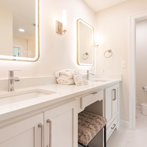 The master bath features elegant dual sinks, bright lighting, a vanity stool, and plush towels for a refreshing retreat