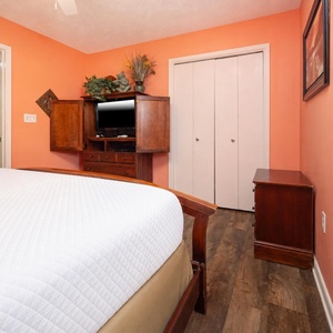 Bright orange walls complement the king bed in and provide a cozy guest room, featuring a TV and ample storage space