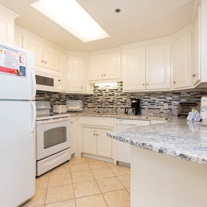 Prepare meals in this kitchen featuring granite counters, white appliances, and stylish tile accents