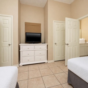 Stylish guest room featuring two double beds, a dresser with a TV, and an adjoining bathroom with neatly stacked towels
