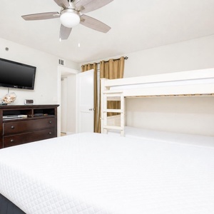 This cozy bedroom features a comfortable queen bed, a twin bunk bed for extra guests, and a wall-mounted TV for entertainment