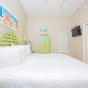 Bright green headboard featuring a king bed in this cozy bedroom, featuring a TV and cheerful beach-themed artwork