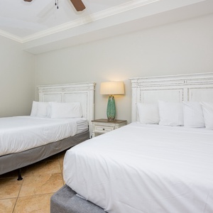 This guest bedroom features two comfortable queen beds, soft white linens, and a stylish lamp, perfect for a restful stay