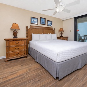 Master bedroom featuring a king bed, wooden furniture, and sliding glass doors leading to the balcony with a beach front view