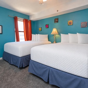 This bright guest bedroom features two full beds, bright blue walls, and cheerful artwork, perfect for a relaxing stay