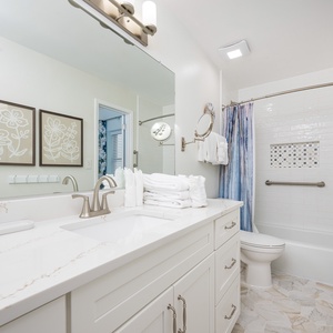 Guest bathroom featuring a marbld countertop, elegant fixtures, and a tub/shower combo with a decorative tile accent