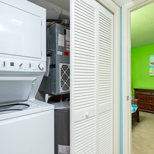 A stacked washer and dryer are visible in a compact laundry area, leading to a vibrant green guest bedroom with beach decor