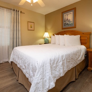 Inviting guest bedroom features a queen bed with crisp white linens, and warm wood accents, for a serene vibe
