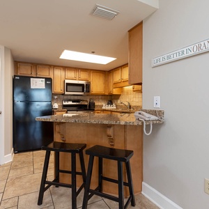 A well-equipped kitchen features wooden cabinetry, granite countertops, and a breakfast bar with two black stools