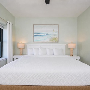 Guest suite invites you to rest on a king bed while coastal views peek through the window nearby