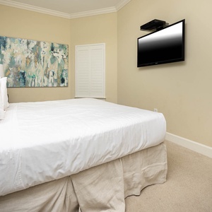 This cozy bedroom features a large king bed, a flat-screen TV, and a vibrant abstract painting, perfect for relaxation