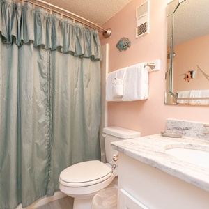 This bathroom features a light pink decor, a marble countertop, and a relaxing shower area with a soft green curtain