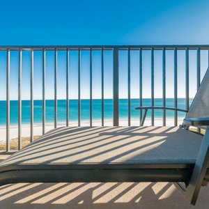 Lounging chair on a balcony offers a serene view of the tranquil gulf and white sand beach, perfect for relaxation