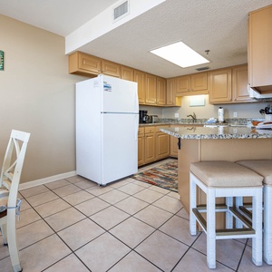 Bright kitchen area featuring granite countertops, a white refrigerator, and a breakfast bar with cushioned seating