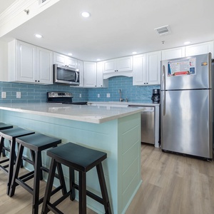 Bright kitchen features a large island with seating, modern cabinetry, and a stylish backsplash, creating a welcoming space