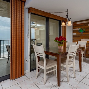 Dining area with a view of the waves, featuring a glass table, stylish chairs, and vibrant floral decor