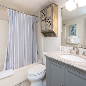 Bright and inviting bathroom featuring a stylish granite countertop, a shower curtain with blue stripes, and elegant decor