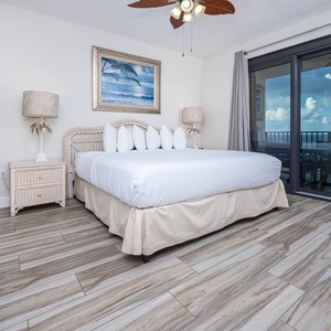 Master bedroom featuring a king bed, wicker nightstands, and sliding glass doors leading to a balcony beach view