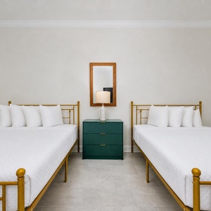 Rest comfortably in this guest room featuring two gold-framed queen beds and a stylish nightstand
