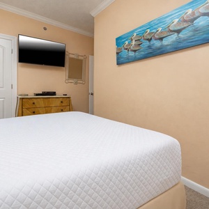 Brightly colored artwork enhances the cozy ambiance of this guest bedroom, featuring a TV and a stylish dresser