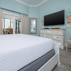 The master bedroom features a calming blue hue, a large TV, and a view through sliding doors to a dining area