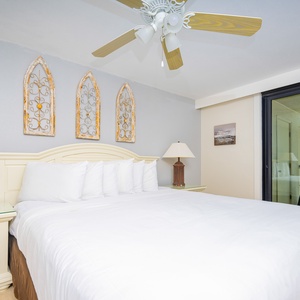 The master bedroom features a plush king bed, decorative wall art, and a balcony with a beautiful view of the beach