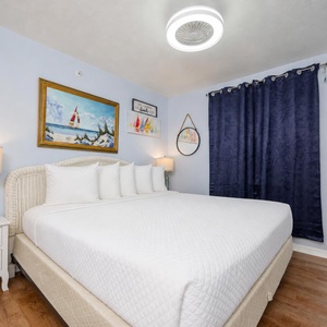 The master bedroom features a comfortable bed, beach-themed decor, and a bright, cheerful atmosphere