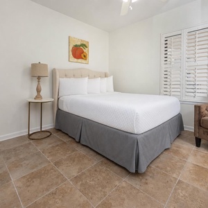 Rest in this serene guest bedroom featuring a plush queen bed, soft linens, and a cozy chair for relaxation
