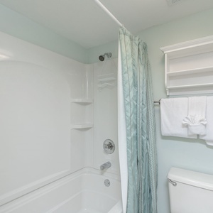 Refreshing master bath featuring a tub/shower combo with soft blue accents and plush white towels for a relaxing stay