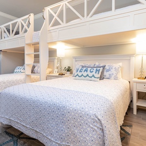 Guests will rest peacefully in this charming bunk room with two twins lofted above two fluffy queen beds