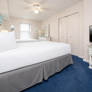 The guest bedroom features two double beds, a TV on a white stand, and a charming dresser with coastal decor accents