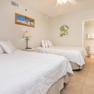 Comfortable guest bedroom featuring two queen beds, soft white linens, and cheerful artwork, creating a relaxing atmosphere