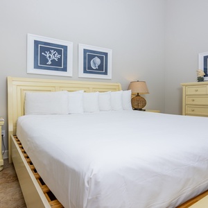 This guest bedroom features a yellow wood king bed, decorative coral art, and soft lighting for a relaxing atmosphere