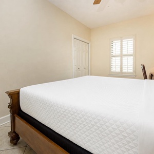 Inviting guest bedroom featuring a large king bed, warm lighting, and a window with plantation shutters for a cozy atmosphere