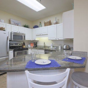 Bright kitchen featuring white cabinetry, granite countertops, and a breakfast bar with nautical-themed decor