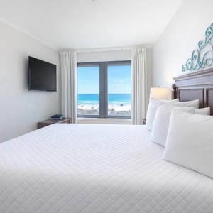 Master suite featuring a plush king bed and a stunning beachfront view through large windows, perfect for relaxation