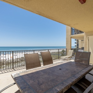The spacious balcony features a dining table with chairs, offering a direct view of the beach and tranquil blue waters