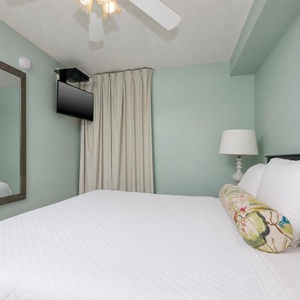 Peaceful bedroom suite featuring a large king bed, a TV for entertainment, and soft teal walls for a calming atmosphere