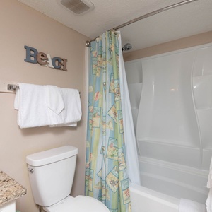 Refreshing guest bath featuring a tub/shower combo, granite countertop, and beach-themed decor for a relaxing retreat