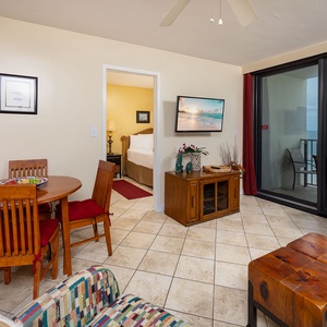 Cozy living area featuring a dining table, colorful couch with queen sleeper, and a view of the beach through balcony doors