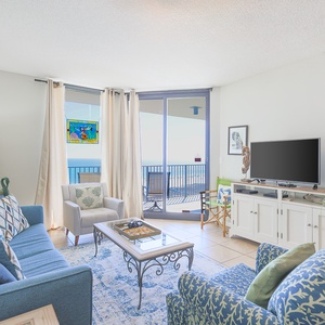 Cozy living area features a blue sofa with queen sleeper, accent chairs, and a view of the beach through sliding glass doors