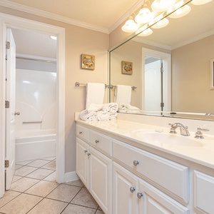Bright master bathroom featuring a spacious vanity, fresh towels, and a tub/shower combo, complemented by decorative art