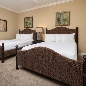 This guest bedroom features two stylish queen beds, soft beige walls, and colorful artwork, creating a relaxing atmosphere