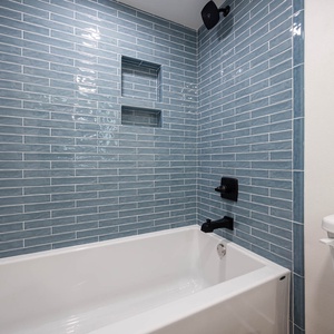 The shower in the guest bath has black fixtures and blue tile accents, complemented by a white tub for a refreshing vibe