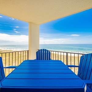 Bright blue chairs surround a table on the balcony, offering a view of the beach and the inviting gulf waters