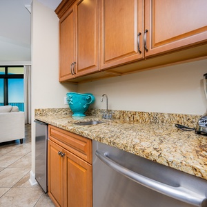 The wet bar features warm wood cabinetry, granite countertops, and a blender, with a view of the beachfront beyond