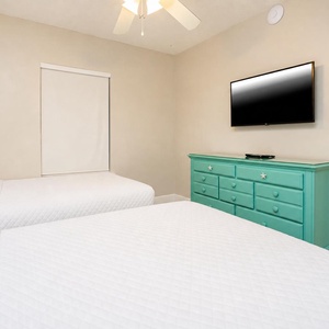 Cozy guest room featuring two comfortable double beds, a vibrant dresser, and a mounted TV for your entertainment