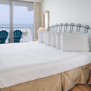 The master bedroom features a plush bed and opens to a stunning beachfront view with cozy seating on the balcony