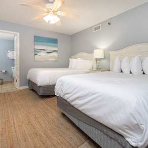 Brightly decorated guest room featuring two double beds, a cozy rug, and a private bathroom visible through the door