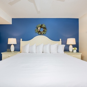 A serene bedroom features a large king bed, decorative pillows, a blue accent wall, and stylish bedside lamps